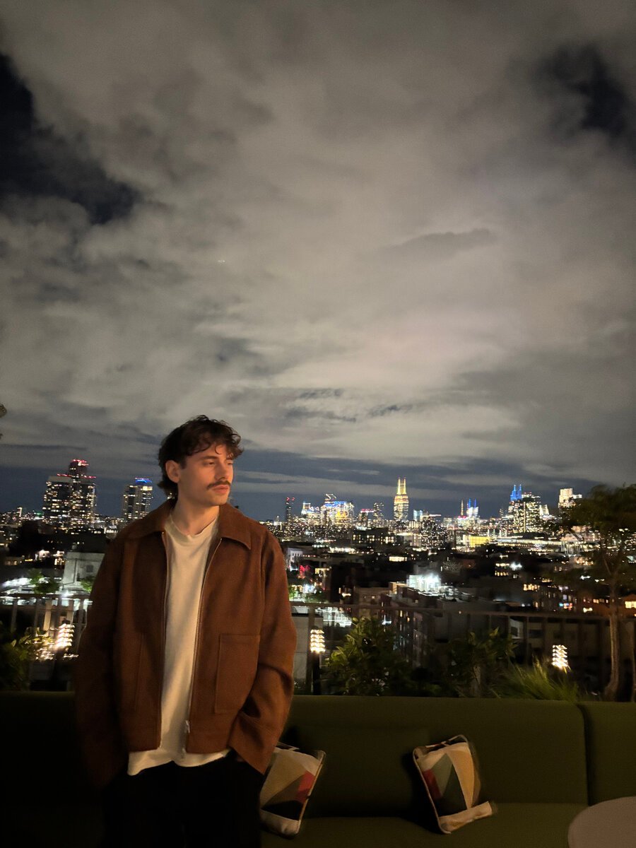 Adrian Bellaire on a rooftop at night, with a city skyline behind him